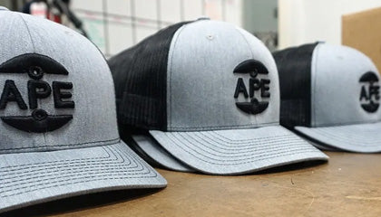 Grey and Black Trucker Caps with 3D Puff Foam embroidery that say APE in black