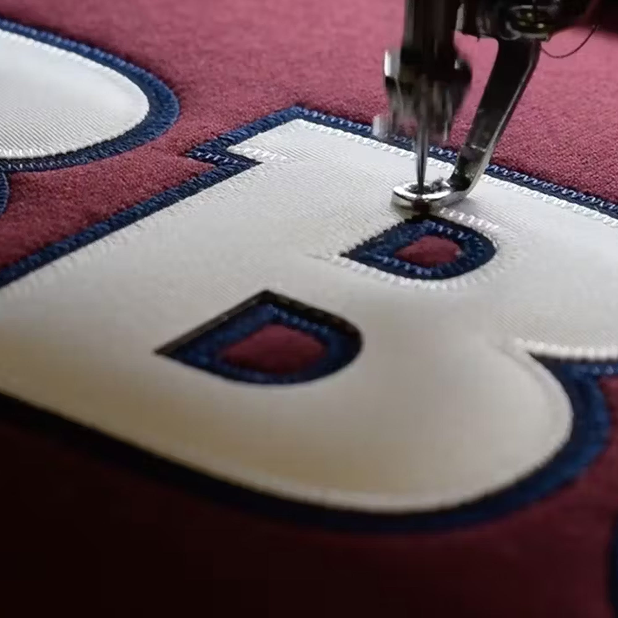 Embroidery machine stitching into a custom tackle twill B on a sweater